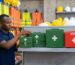 Four first aid kit boxes in ascending sizes, three green metal boxes and one red plastic box, on a shop shelf in Nairobi with hi-vis vests and hard hats in the background