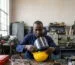 A Black Kenyan worker fitting a clear polycarbonate visor onto a safety helmet visor carrier